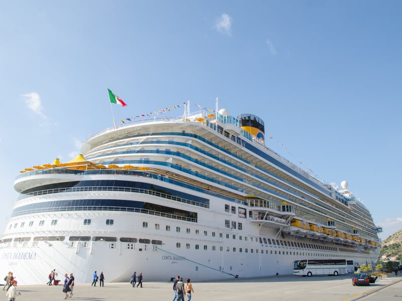 A large cruise ship moored at the quay of the port of Gruž in Dubrovnik, with passengers walking along the pier