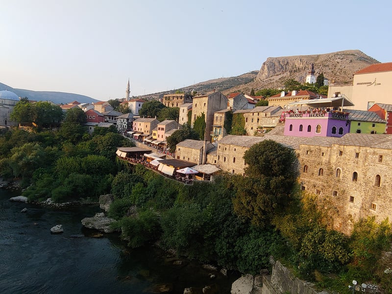 Mostar's old town and the Neretva river at sunset, with a minaret and the hills behind